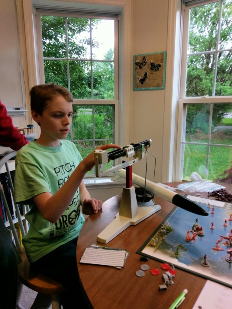 teen boy sitting at a table weighing a homemade rocket on a triple beam balance
