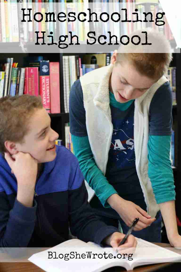 Homeschooling High School - two teens at a table, one sitting and one standing to help each other and discuss work