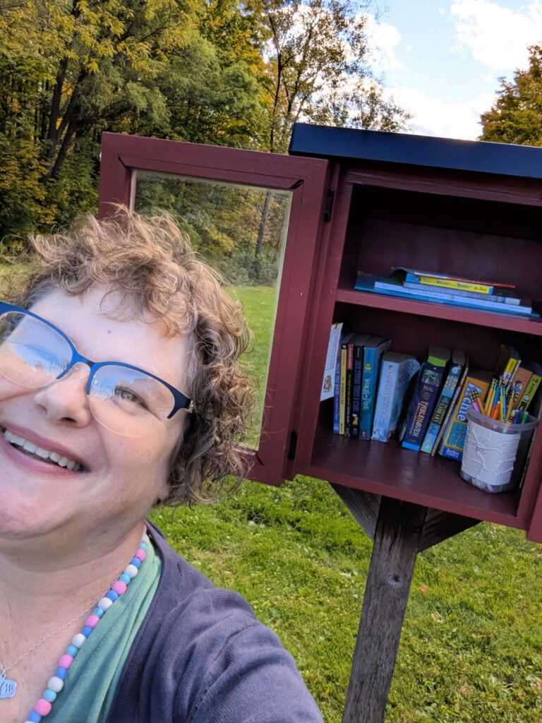 Woman in front of a Little Free Library leaning into a selfie